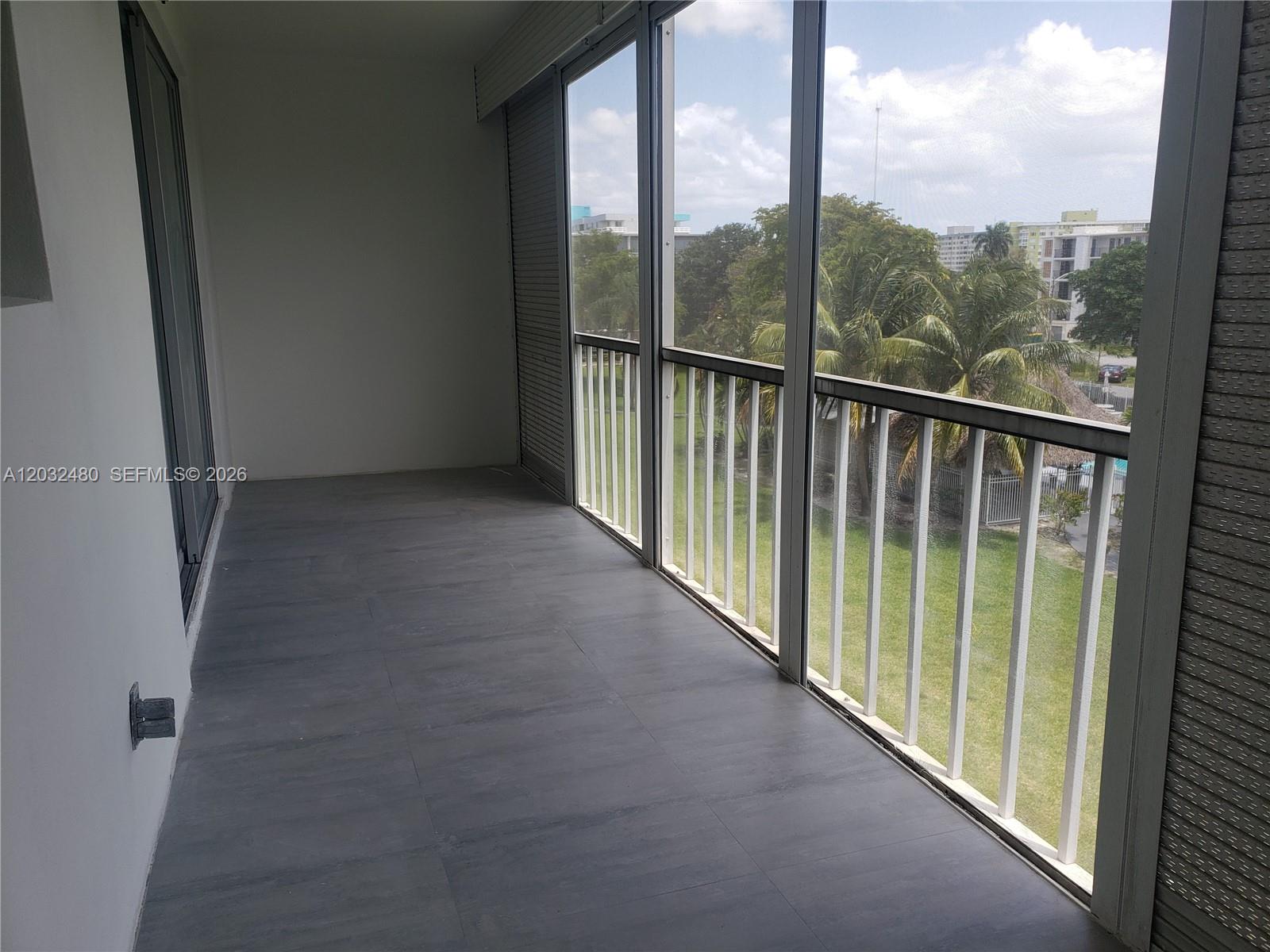 A screened-in balcony features gray tile flooring and white railings overlooking a grassy area — 4700 Washington St # 404, Hollywood FL 33021, HOLLYWOOD, FL