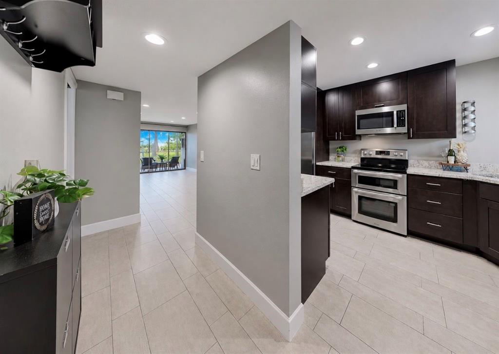 A kitchen with dark cabinets and stainless steel appliances opens to a light-filled living area — 1028 APOLLO BEACH BOULEVARD UNIT 102, APOLLO BEACH, FL