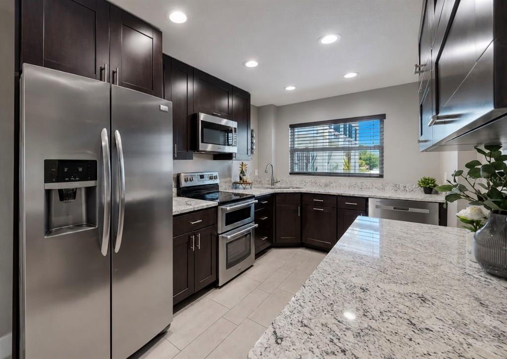 A kitchen features dark wood cabinets, stainless steel appliances, and light granite countertops — 1028 APOLLO BEACH BOULEVARD UNIT 102, APOLLO BEACH, FL