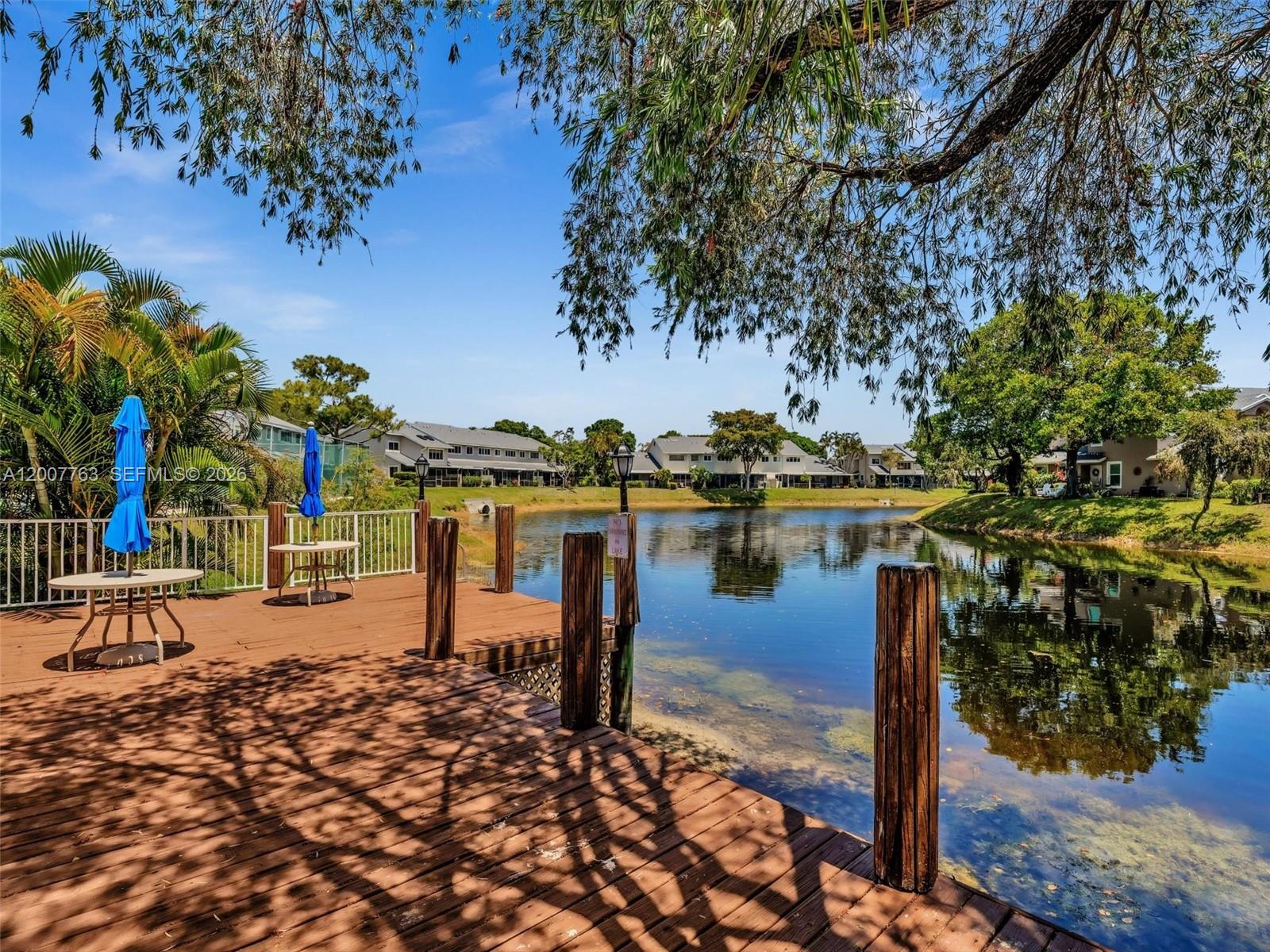 A wooden deck overlooks a lake with residential buildings in the background — 1958 E Discovery Cir E, Deerfield Beach FL 33442, DEERFIELD BEACH, FL