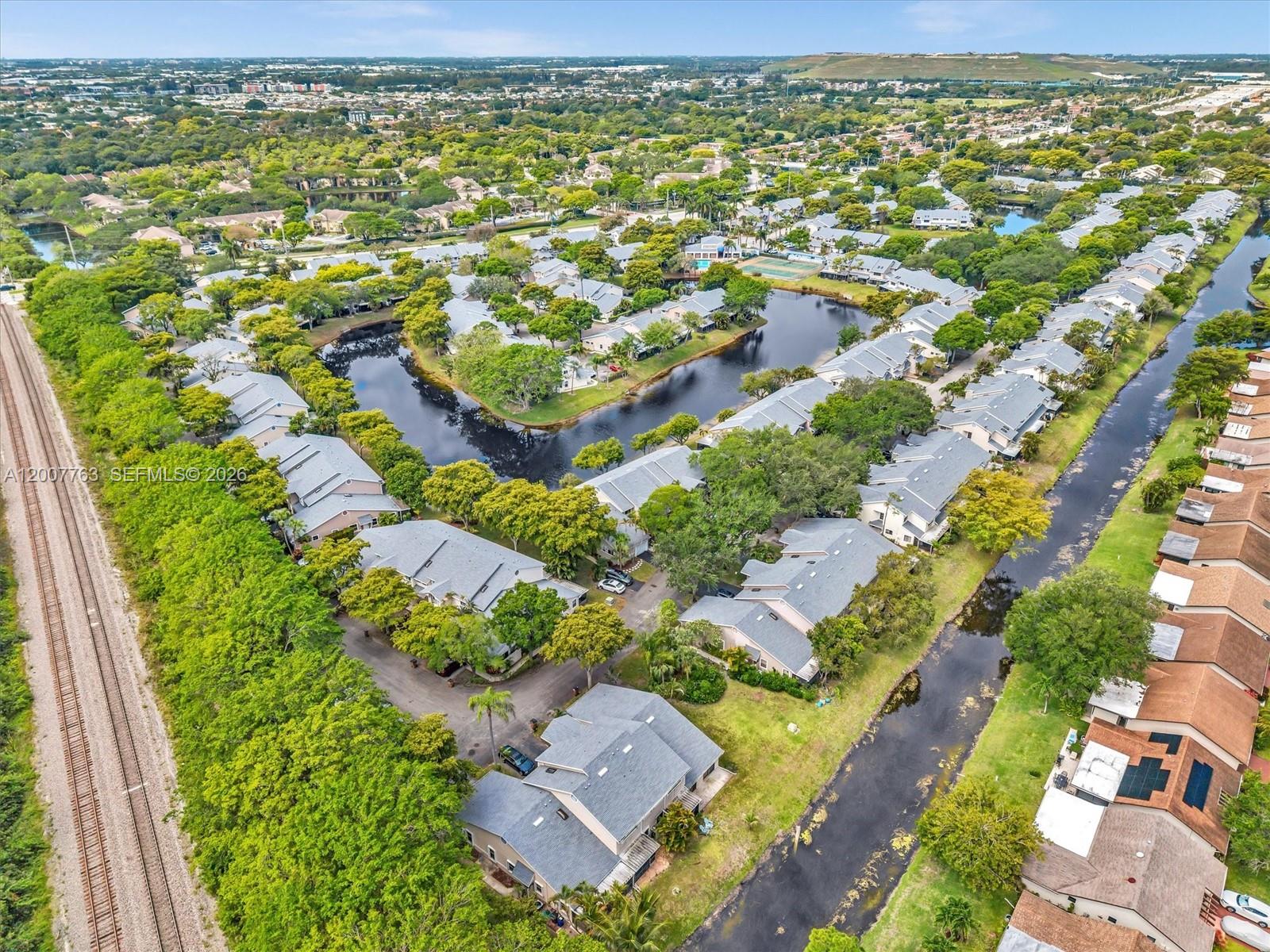 An aerial view shows residential townhomes situated along a canal next to railroad tracks — 1958 E Discovery Cir E, Deerfield Beach FL 33442, DEERFIELD BEACH, FL