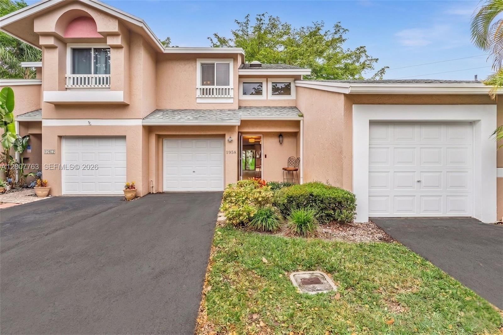 A two-story peach-colored townhouse features three garage doors and a small front garden — 1958 E Discovery Cir E, Deerfield Beach FL 33442, DEERFIELD BEACH, FL