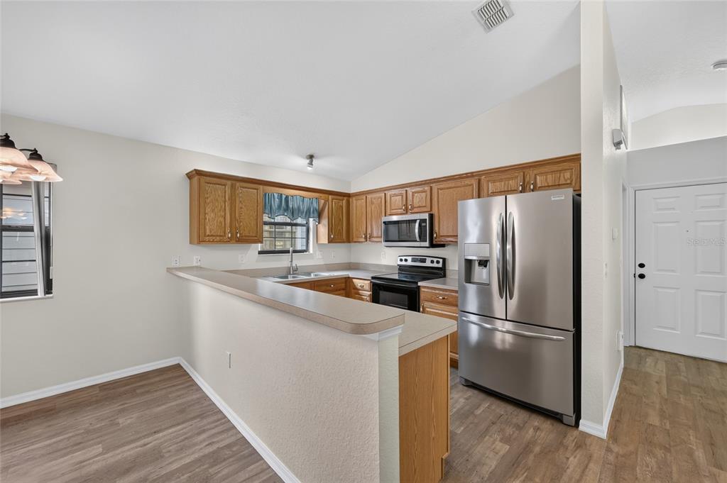 A kitchen with wood cabinets, stainless steel appliances, and a breakfast bar overlooking the room — 3928 NE 22ND STREET, OCALA, FL