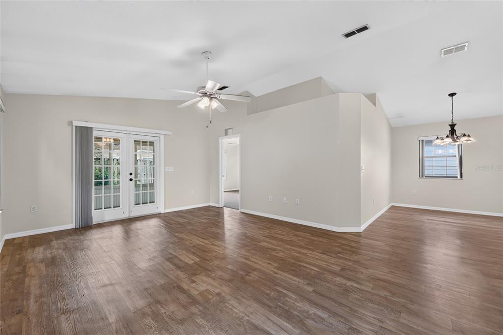 A spacious living room features light walls, wood-look flooring, a ceiling fan, and glass doors — 3928 NE 22ND STREET, OCALA, FL