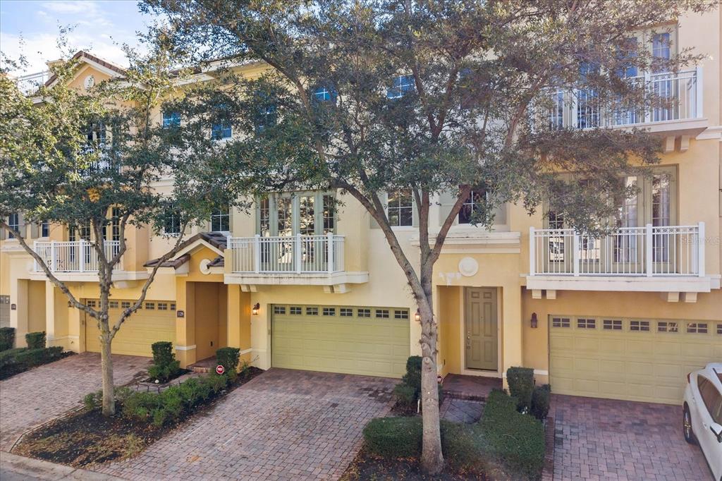 An exterior view of a multi-story townhouse complex with beige stucco walls and paved driveways — 1125 BOLTON PLACE, LAKE MARY, FL