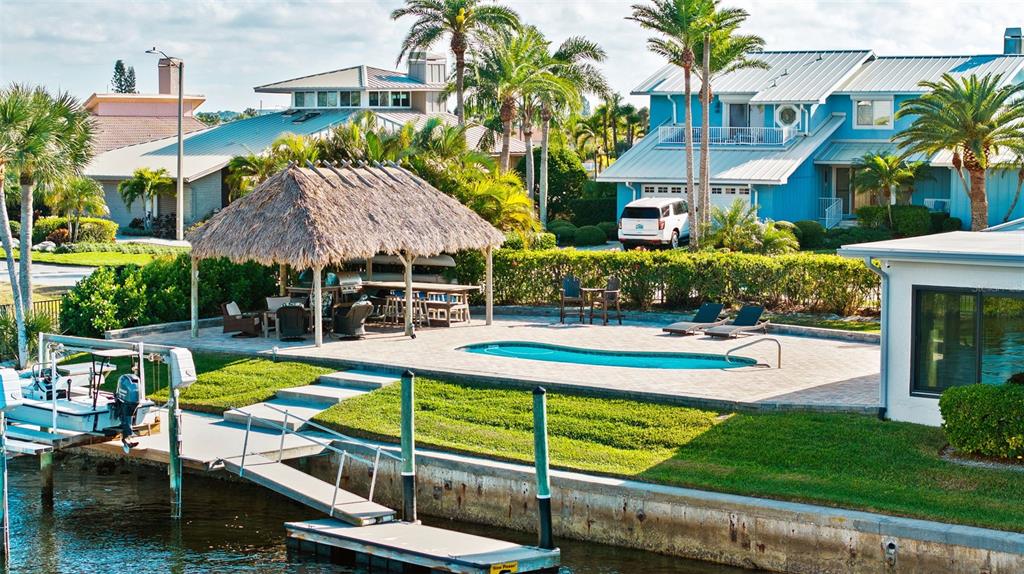 A waterfront backyard features a pool, a thatched-roof tiki bar, and a private boat dock — 5791 WESTSHORE DRIVE, NEW PORT RICHEY, FL