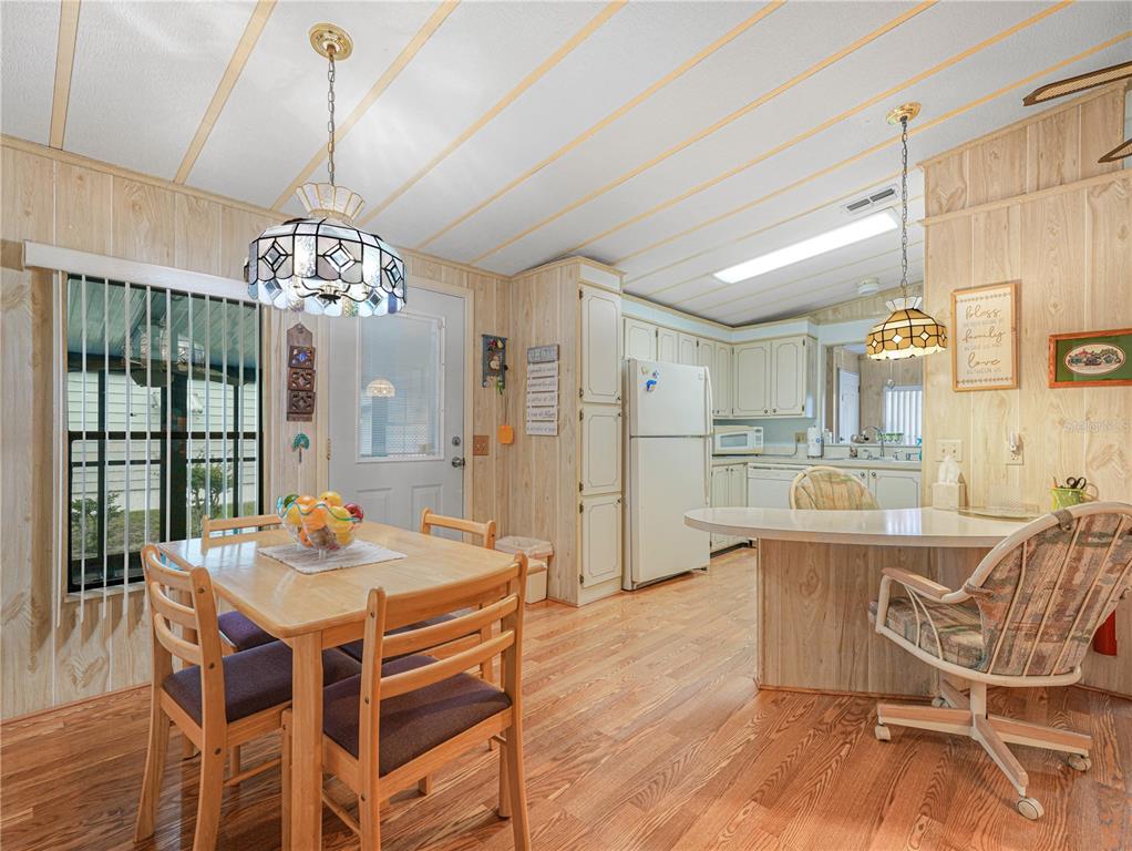 A kitchen and dining area featuring wood-paneled walls, light wood flooring, and two pendant lights — 108 KENSINGTON PARK DRIVE, DAVENPORT, FL