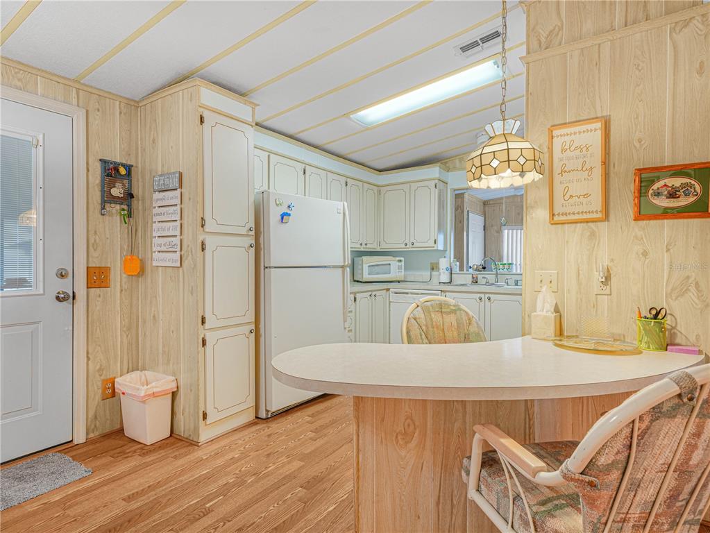 A kitchen with wood-paneled walls, white cabinets, a white refrigerator, and a curved breakfast bar — 108 KENSINGTON PARK DRIVE, DAVENPORT, FL