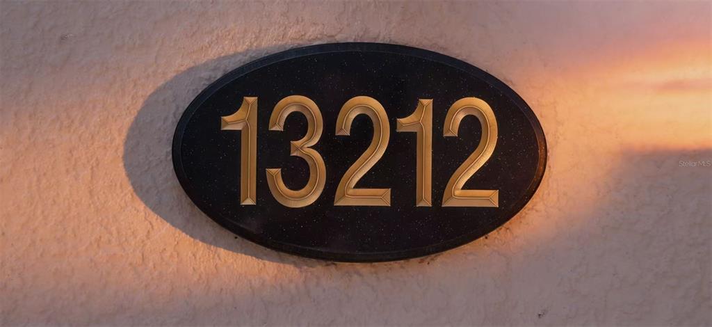 A black oval plaque with gold house numbers is mounted on a textured stucco wall — 13212 SOCIAL LANE, WINTER GARDEN, FL