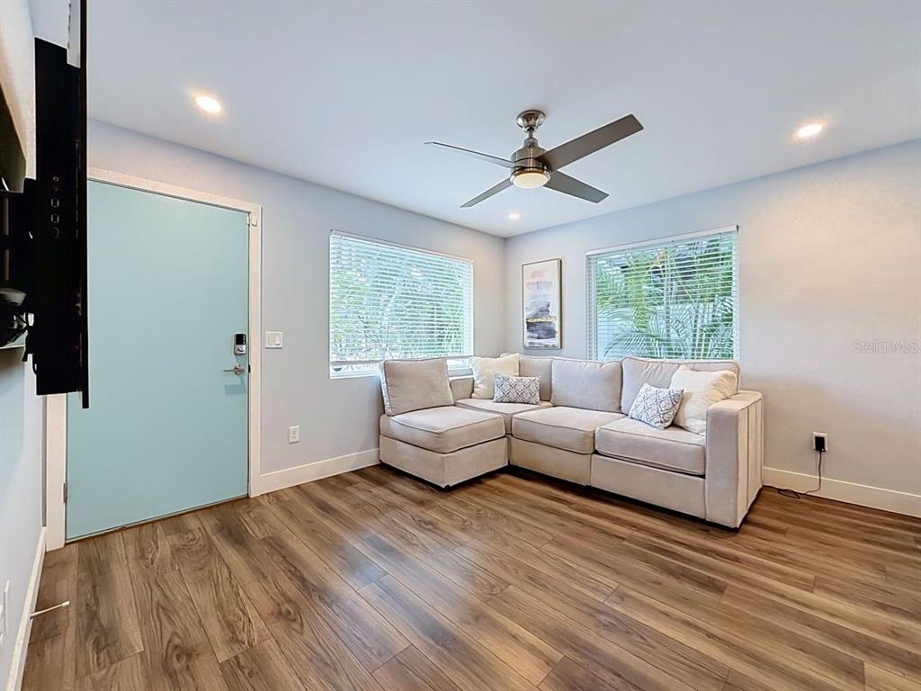 A living room features a light-colored sectional sofa, wood-look flooring, and a light blue door — 5458 6TH AVENUE N, ST PETERSBURG, FL