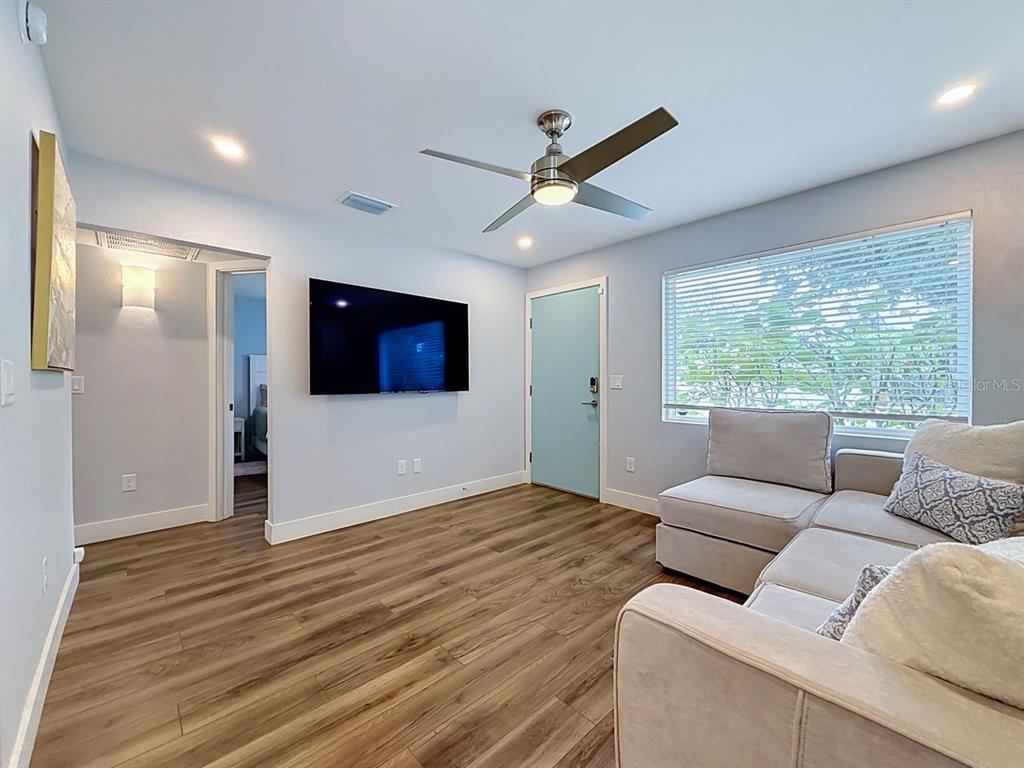 A living room features light blue walls, wood-look flooring, a ceiling fan, and a television — 5458 6TH AVENUE N, ST PETERSBURG, FL