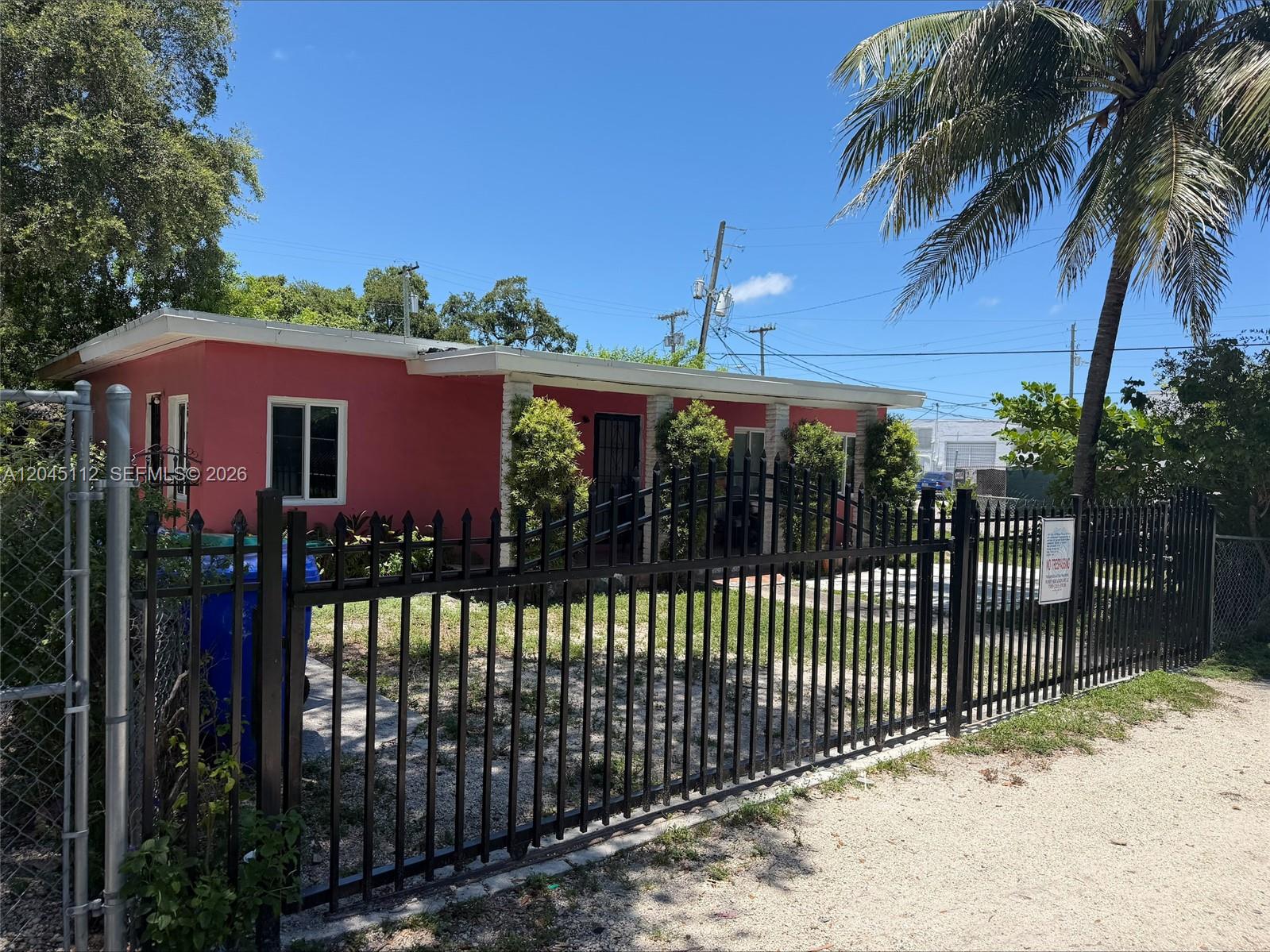 A pink single-story house is viewed from behind a black metal fence under a blue sky — 157 NE 64th Ter, Miami FL 33138, MIAMI, FL
