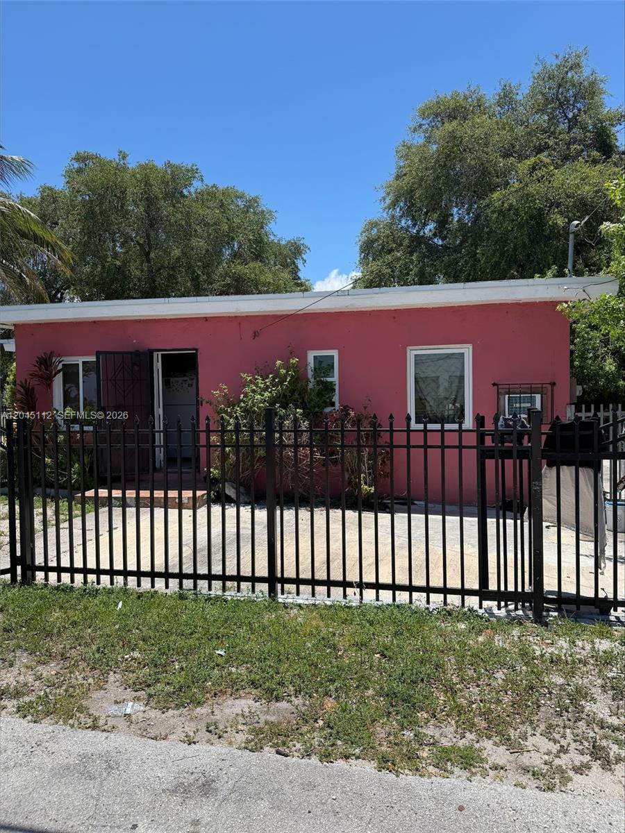 A pink, single-story house is viewed from the street behind a black metal fence — 157 NE 64th Ter, Miami FL 33138, MIAMI, FL