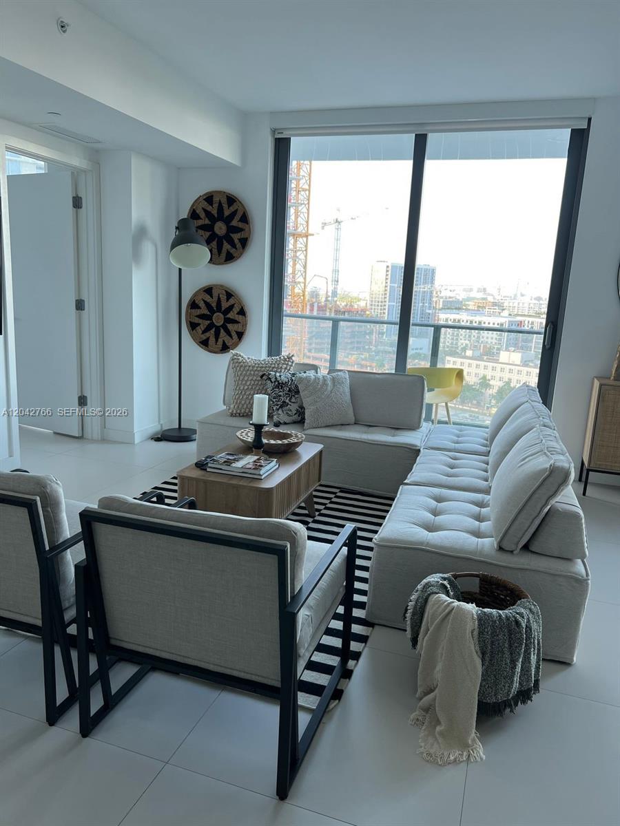 A modern living room features a sectional sofa, armchairs, and floor-to-ceiling windows overlooking city construction — 501 NE 31st St # 1409, Miami FL 33137, MIAMI, FL