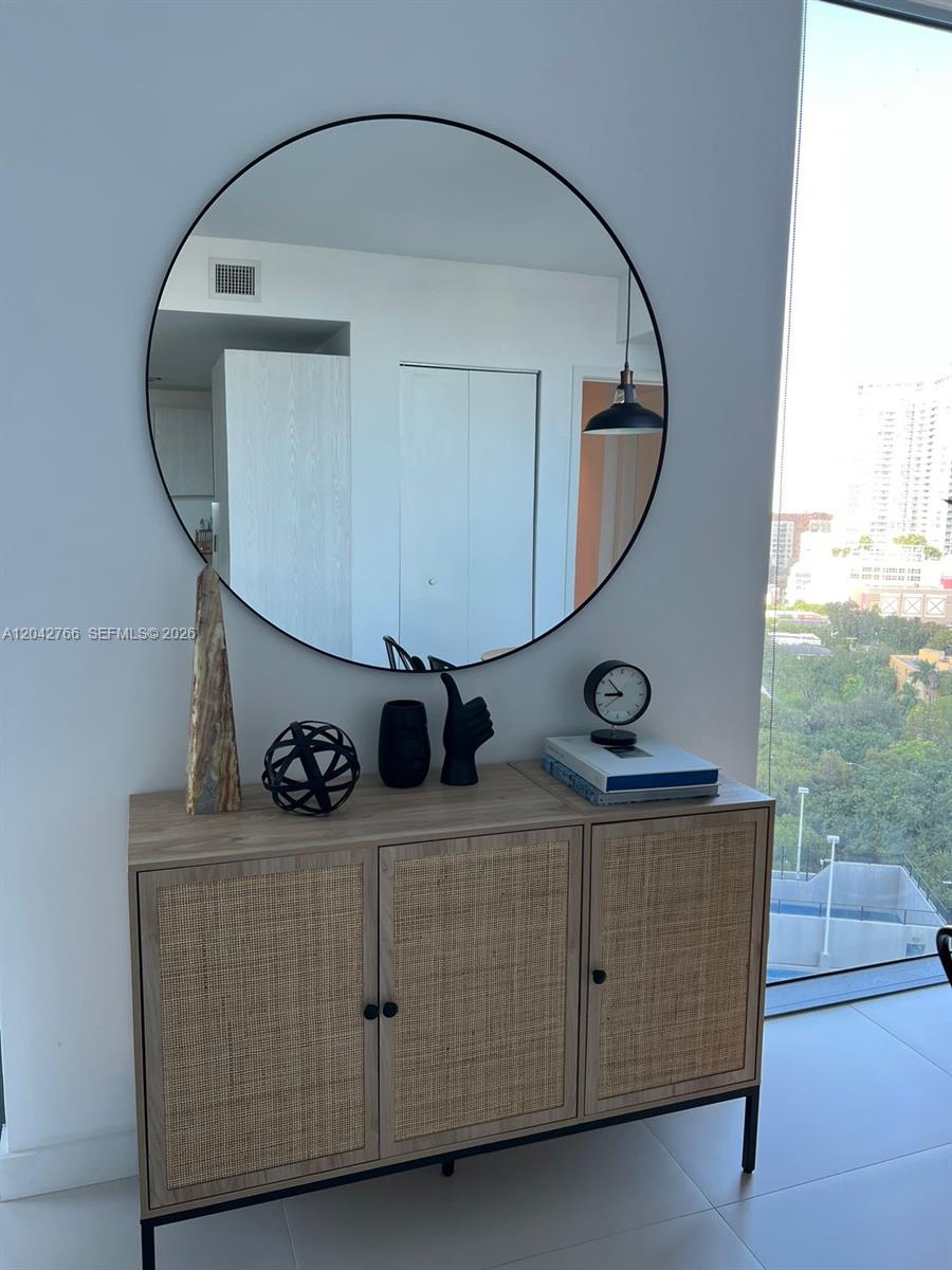 A wooden sideboard with cane doors sits beneath a large round mirror in a room — 501 NE 31st St # 1409, Miami FL 33137, MIAMI, FL