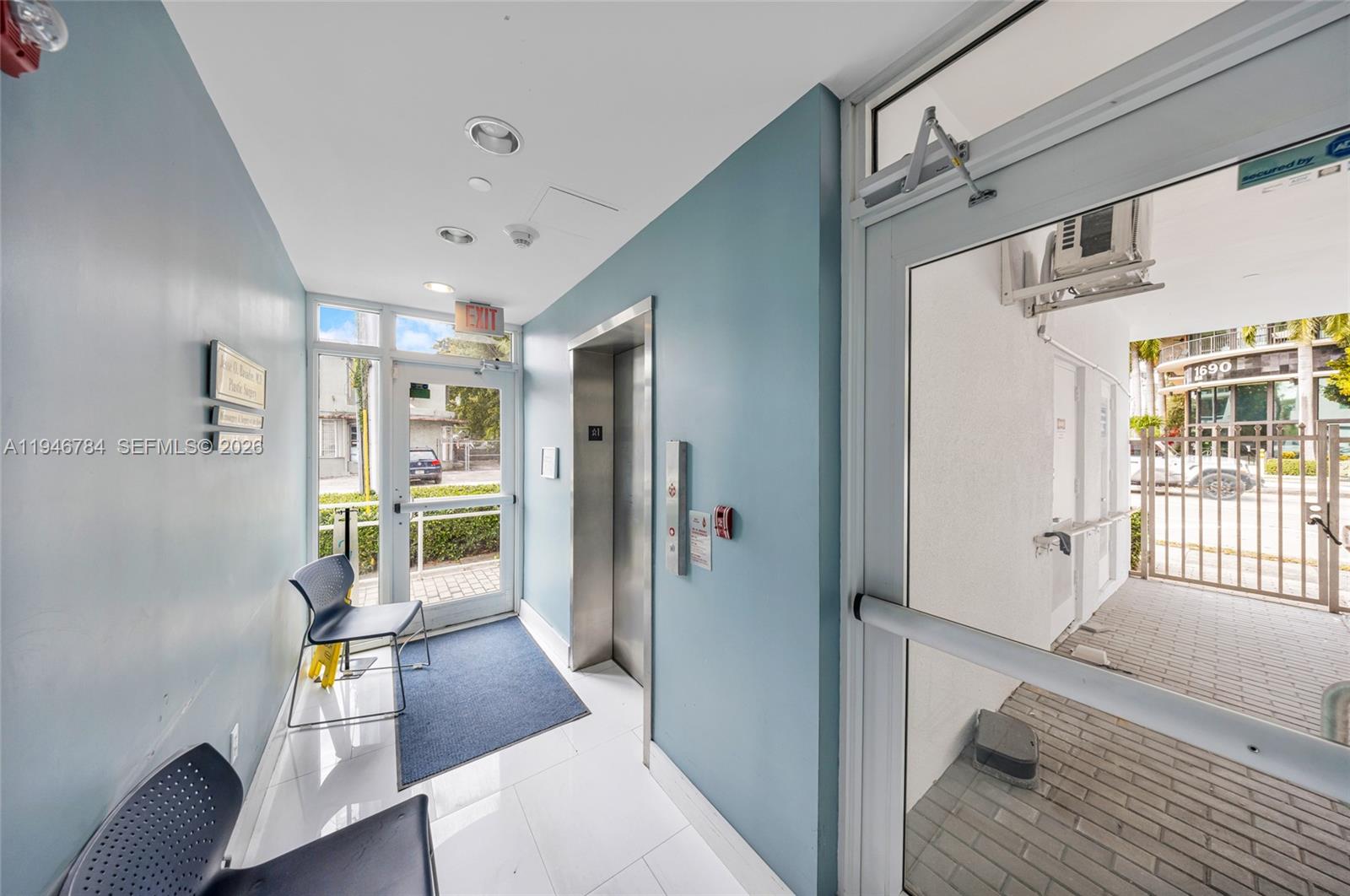 An elevator lobby features blue walls, white tile flooring, two chairs, and a glass exit door — 1693 SW 27th Ave, Miami FL 33145, MIAMI, FL