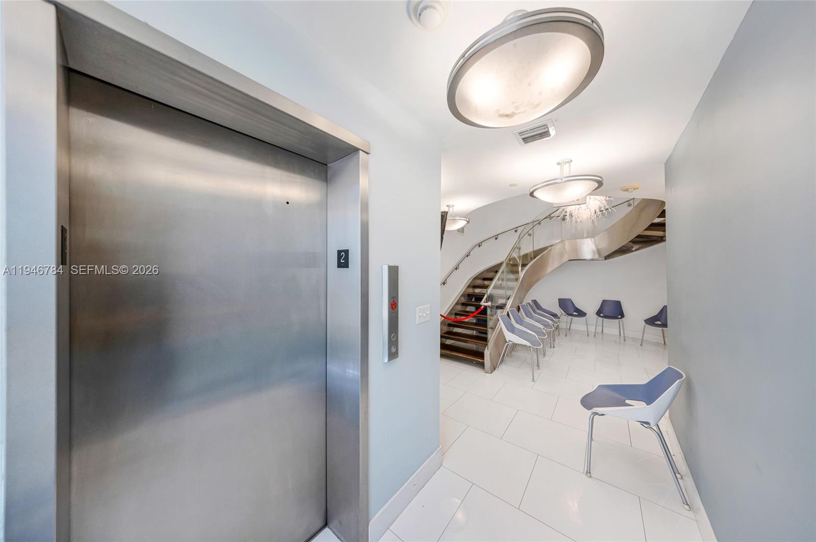 A modern lobby features a stainless steel elevator, a curved staircase, and several blue chairs — 1693 SW 27th Ave, Miami FL 33145, MIAMI, FL