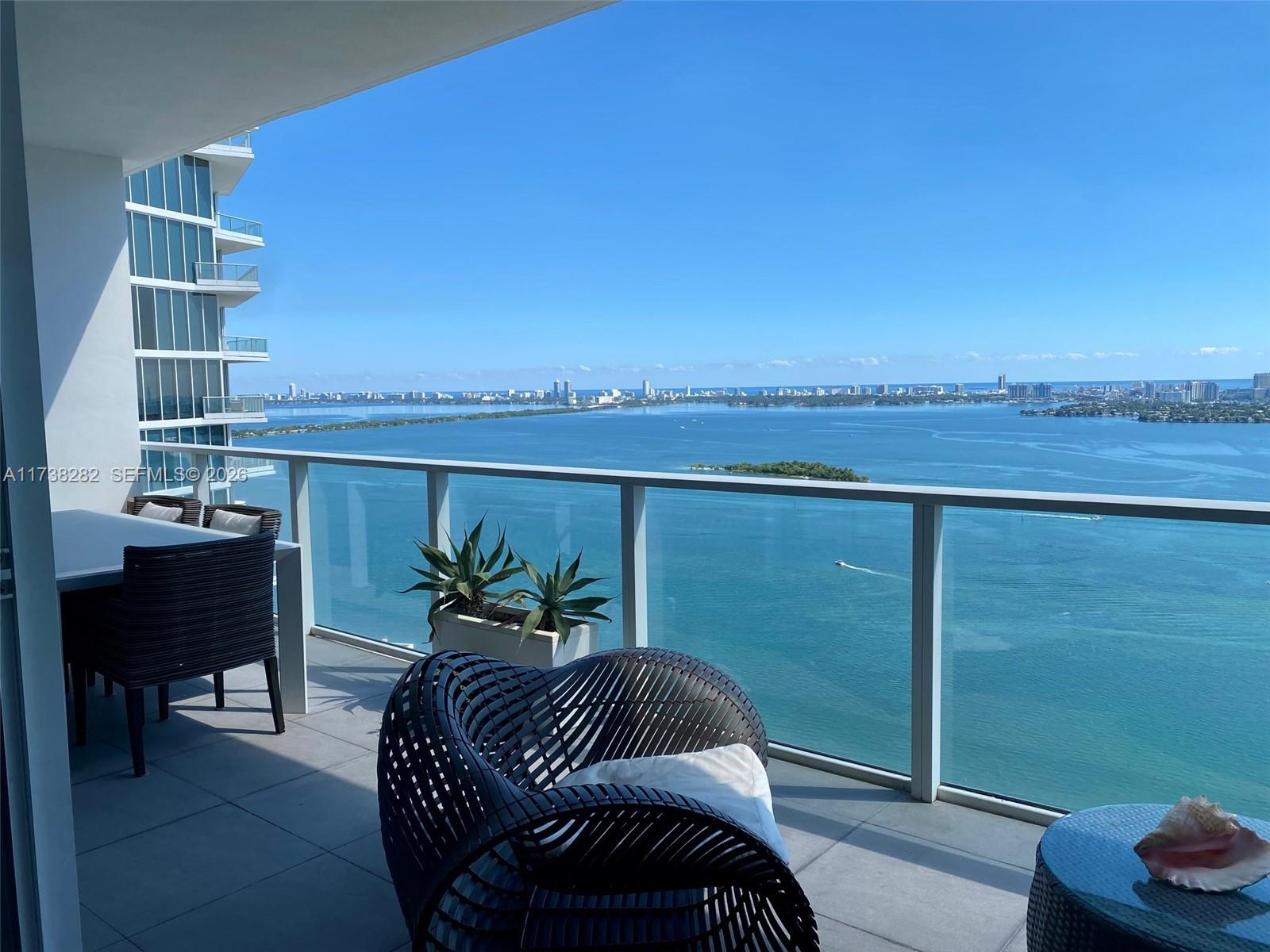 A high-rise balcony features outdoor furniture, a glass railing, and a panoramic bay view — 2020 N Bayshore Dr # 3307, Miami FL 33137, MIAMI, FL