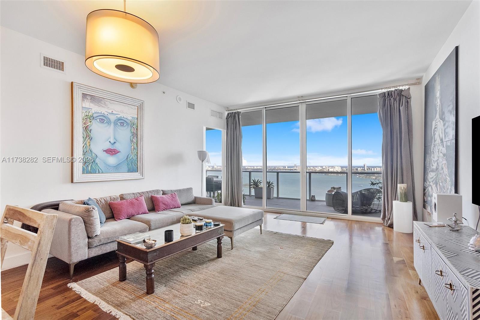 A living room features a gray sectional sofa, a coffee table, and floor-to-ceiling windows overlooking water — 2020 N Bayshore Dr # 3307, Miami FL 33137, MIAMI, FL
