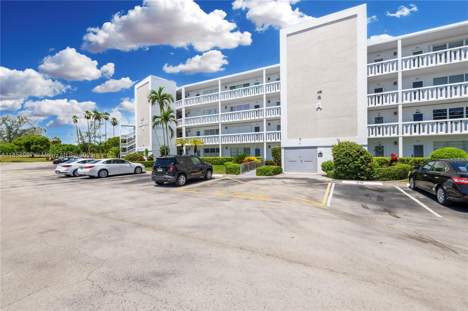 A multi-story white apartment building stands behind a parking lot with several parked cars — 1010 Ellesmere A # 1010, Deerfield Beach FL 33442, DEERFIELD BEACH, FL