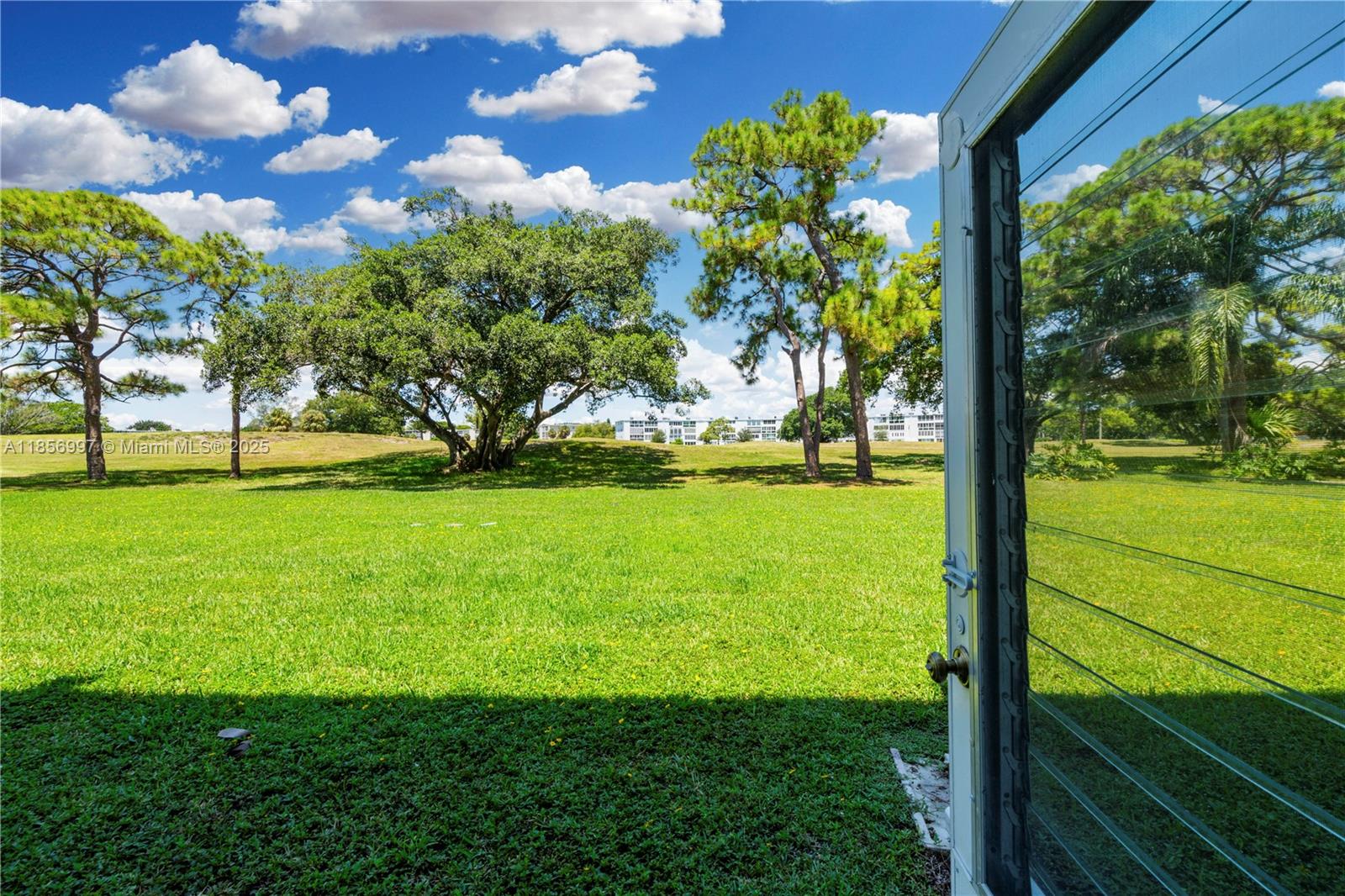 A view of a grassy lawn and trees seen through an open jalousie window — 1010 Ellesmere A # 1010, Deerfield Beach FL 33442, DEERFIELD BEACH, FL