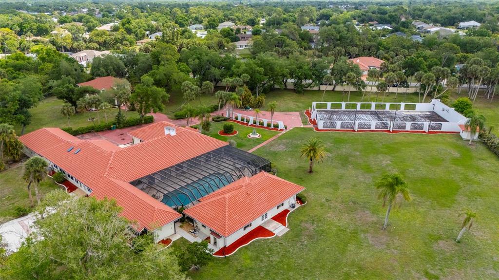 An aerial view shows a house with a red tile roof, pool enclosure, and tennis court — 1105 YORKSHIRE STREET, PORT CHARLOTTE, FL