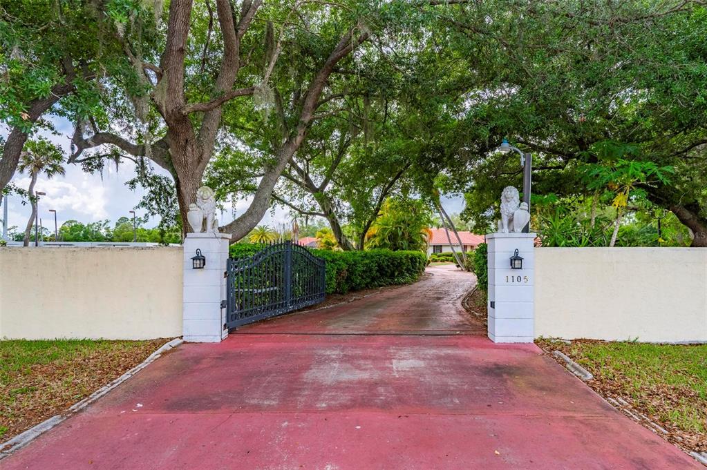 A gated driveway entrance features two white pillars topped with lion statues and large trees — 1105 YORKSHIRE STREET, PORT CHARLOTTE, FL