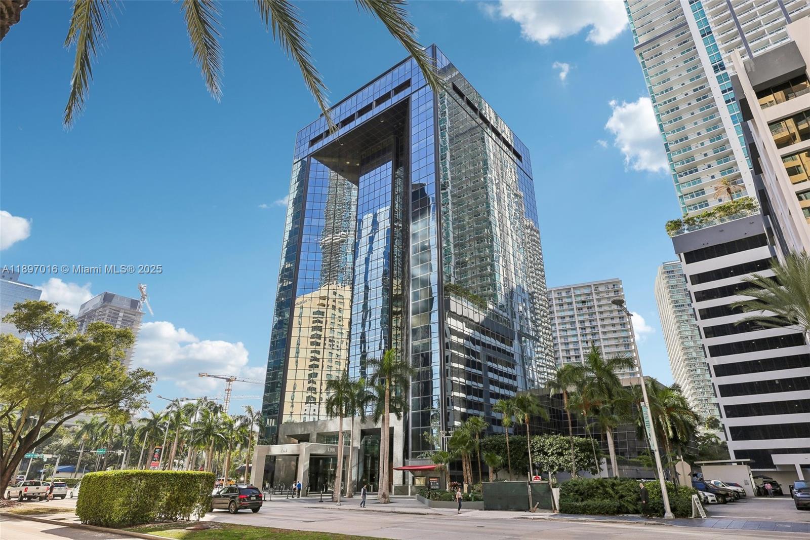 A modern glass-facade high-rise building stands prominently under a clear blue sky — 1200 Brickell Ave # D, Miami FL 33131, MIAMI, FL