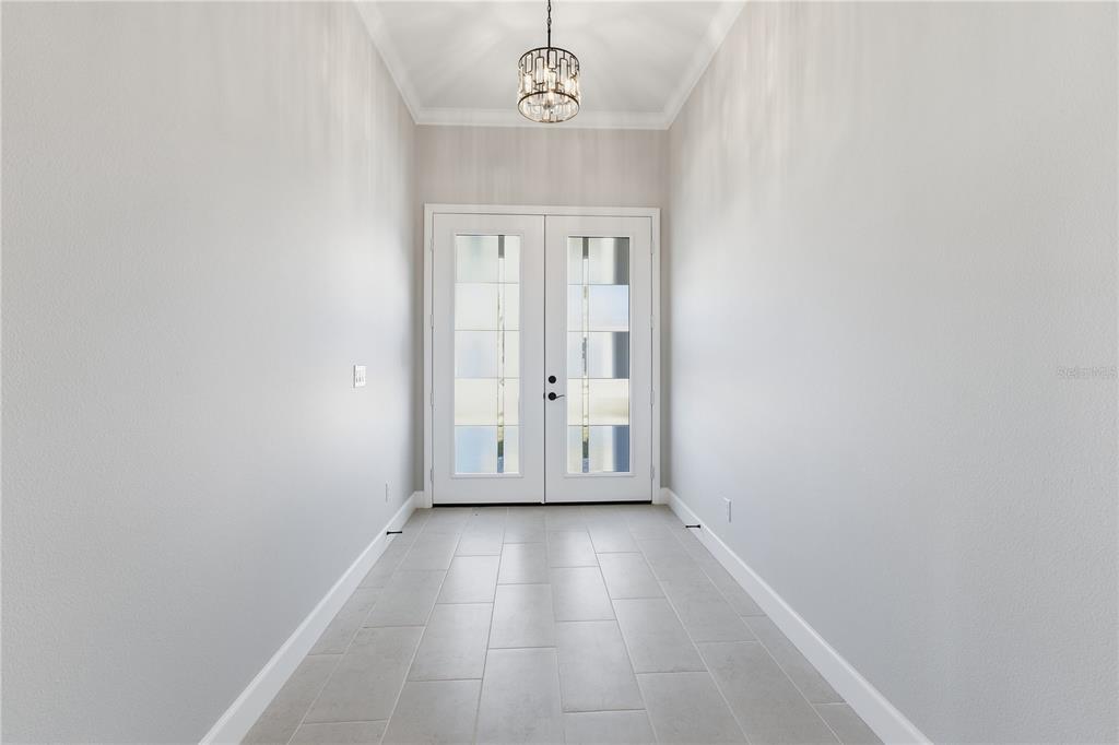 A bright entryway features light gray tile flooring, white walls, and a modern drum chandelier — 721 REDBUD COURT, ENGLEWOOD, FL