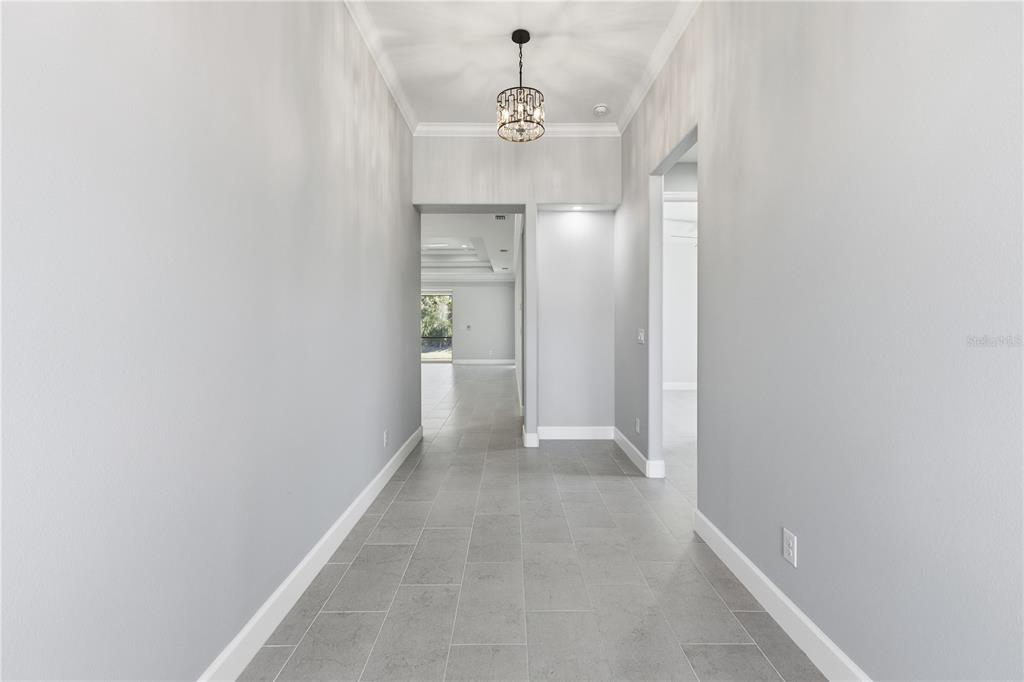 A gray-walled hallway features a crystal chandelier, tile flooring, and an open doorway ahead — 721 REDBUD COURT, ENGLEWOOD, FL
