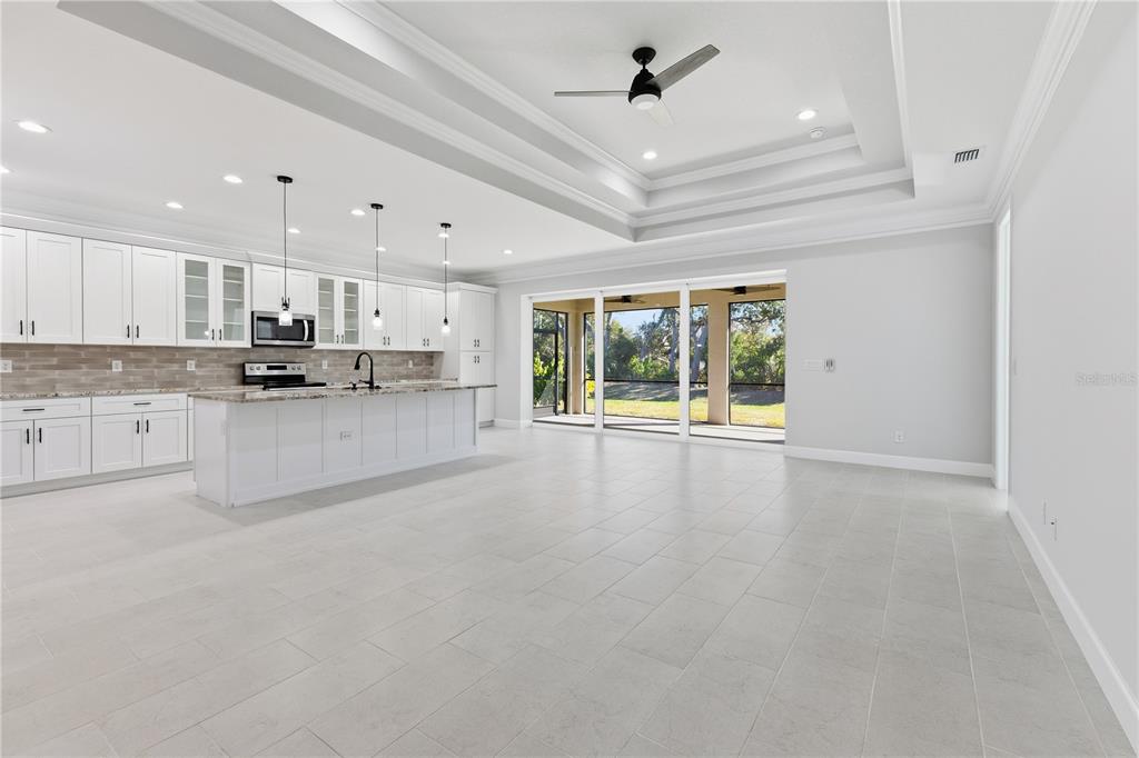 A bright, open-concept kitchen features white cabinetry, a large island, and sliding glass patio doors — 721 REDBUD COURT, ENGLEWOOD, FL