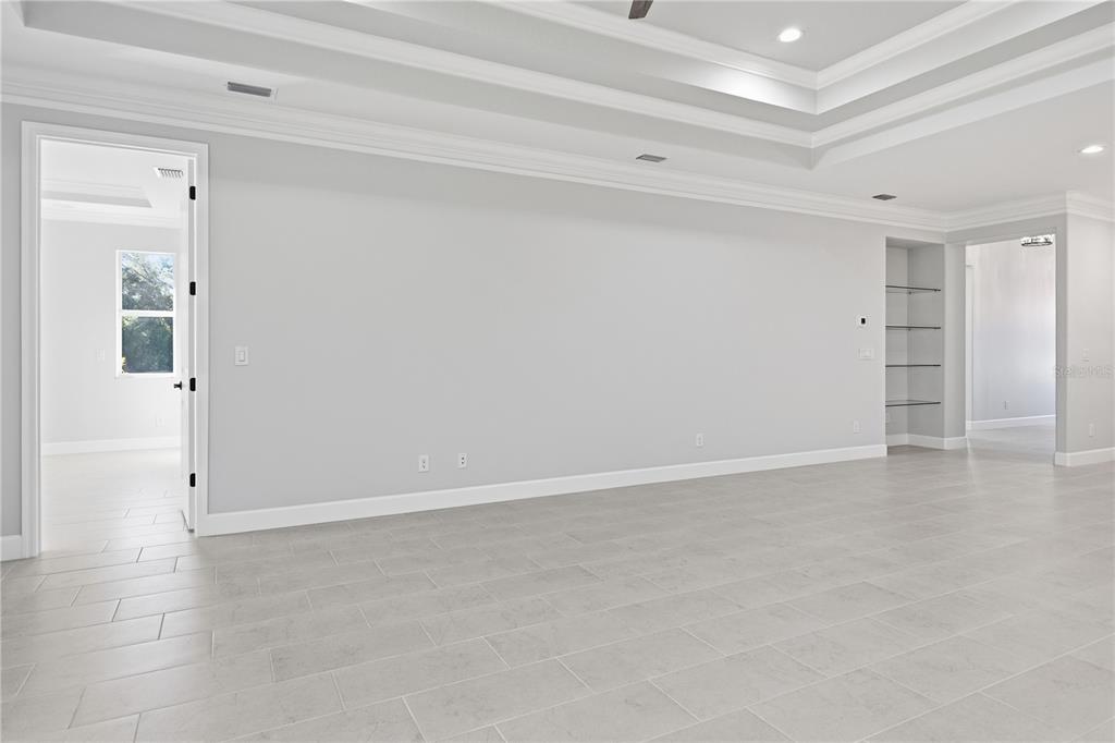 A spacious room with light gray walls, tile flooring, a tray ceiling, and built-in shelving — 721 REDBUD COURT, ENGLEWOOD, FL