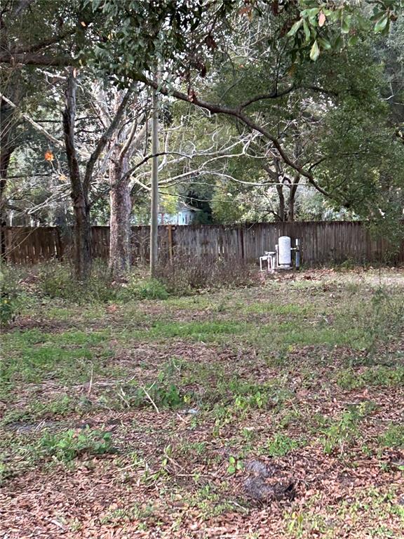 A wooded backyard features a wooden fence and a white well pump assembly — 3633 APFEL ROAD, WESLEY CHAPEL, FL