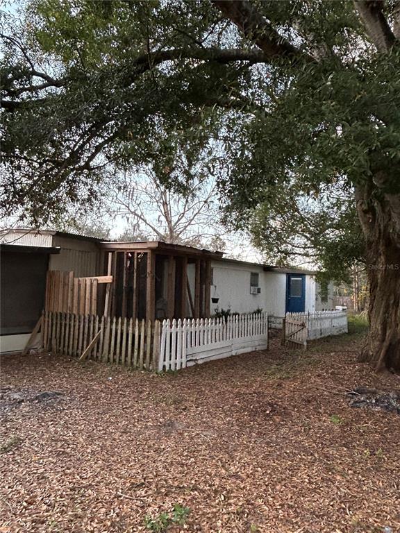 A mobile home with a screened porch and white picket fence sits under large trees — 3633 APFEL ROAD, WESLEY CHAPEL, FL