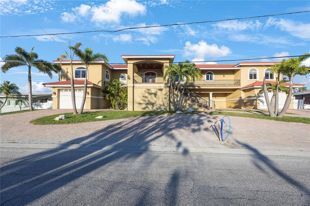 A large, two-story yellow stucco house features a tiled roof, palm trees, and paved driveway — 736 PRUITT DRIVE, MADEIRA BEACH, FL