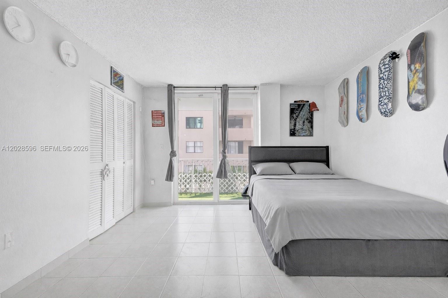 A bedroom features white tile floors, a bed with gray bedding, and skateboards mounted on walls — 7133 Bay Dr # 305, Miami Beach FL 33141, MIAMI BEACH, FL