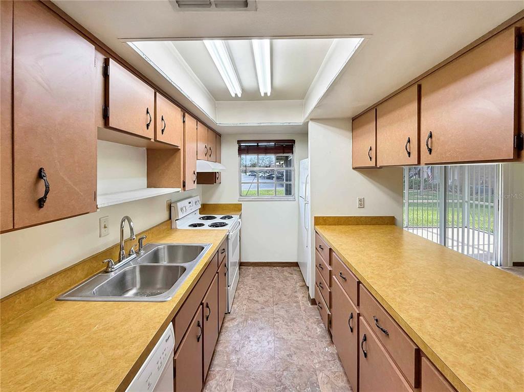 A galley kitchen features wood cabinets, yellow laminate countertops, and a double-basin stainless steel sink — 590 BELLTOWER AVENUE UNIT H, DELTONA, FL