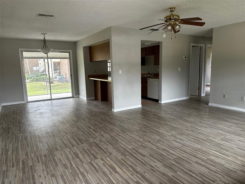 An open-concept living and dining area features wood-look flooring, a ceiling fan, and sliding doors — 590 BELLTOWER AVENUE UNIT H, DELTONA, FL