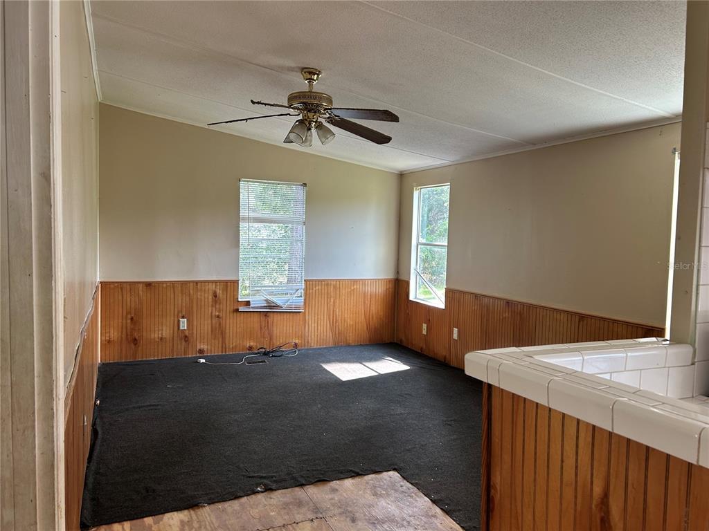 A room with wood paneling, dark carpeting, two windows, and a ceiling fan — 2751 SE STATE ROAD 121, MORRISTON, FL