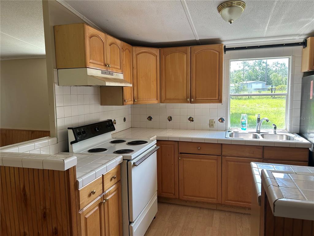 A kitchen features wood cabinets, white tile countertops, a white stove, and a window — 2751 SE STATE ROAD 121, MORRISTON, FL