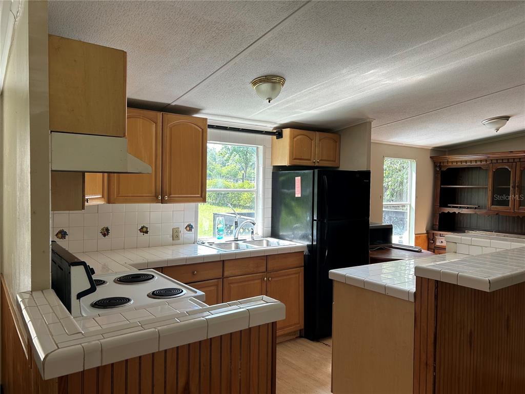 A kitchen with light wood cabinets, white tiled countertops, and a black refrigerator — 2751 SE STATE ROAD 121, MORRISTON, FL