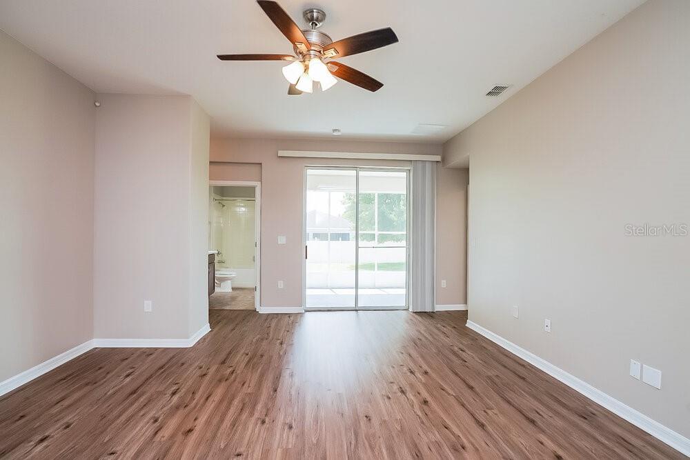 A living room with wood-look flooring, a ceiling fan, and sliding glass doors to a patio — 5736 COQUYT DRIVE, MOUNT DORA, FL