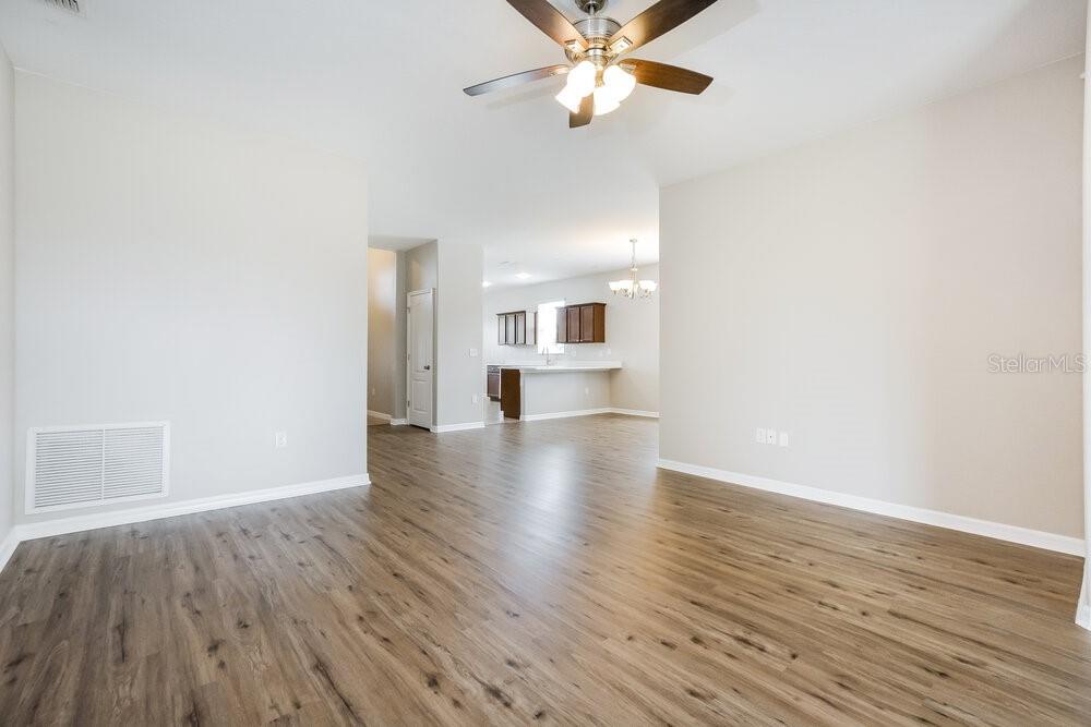 An interior view of a living room with wood-look flooring and an open kitchen beyond — 5736 COQUYT DRIVE, MOUNT DORA, FL