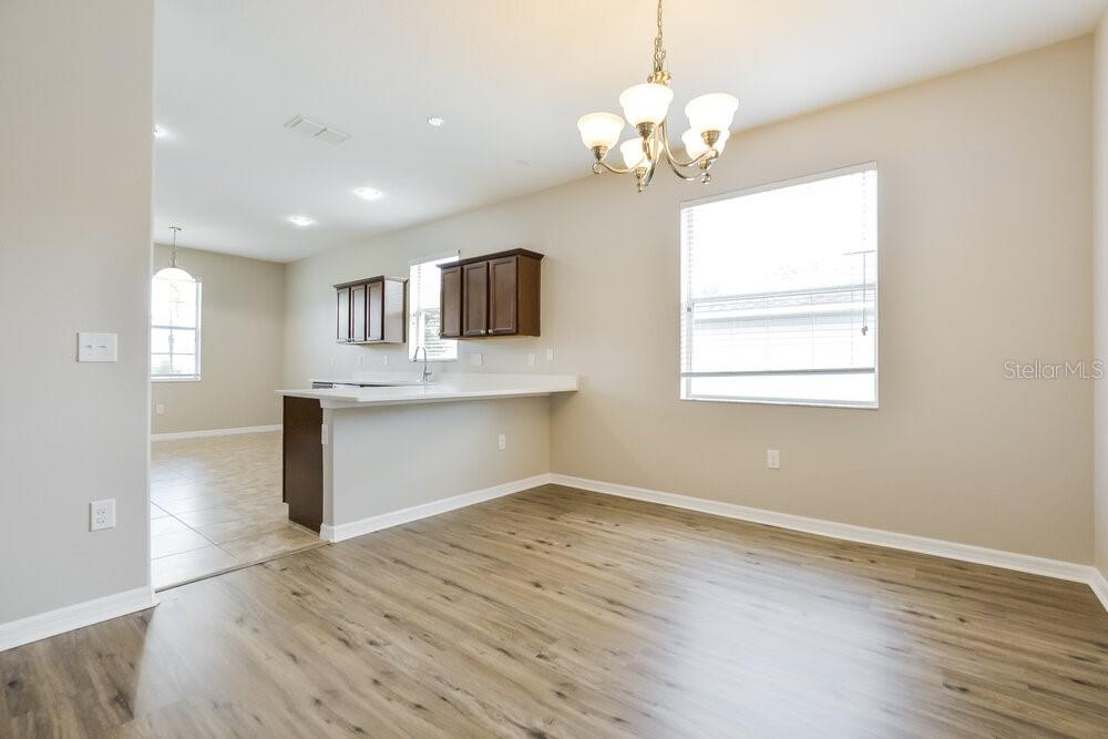 A dining area with wood-look flooring connects to a kitchen featuring dark cabinets and counters — 5736 COQUYT DRIVE, MOUNT DORA, FL