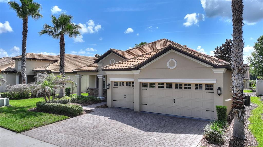 A tan house with a tiled roof, a three-car garage, and palm trees in the yard — 1317 GLENEAGLES LN, DAVENPORT, FL