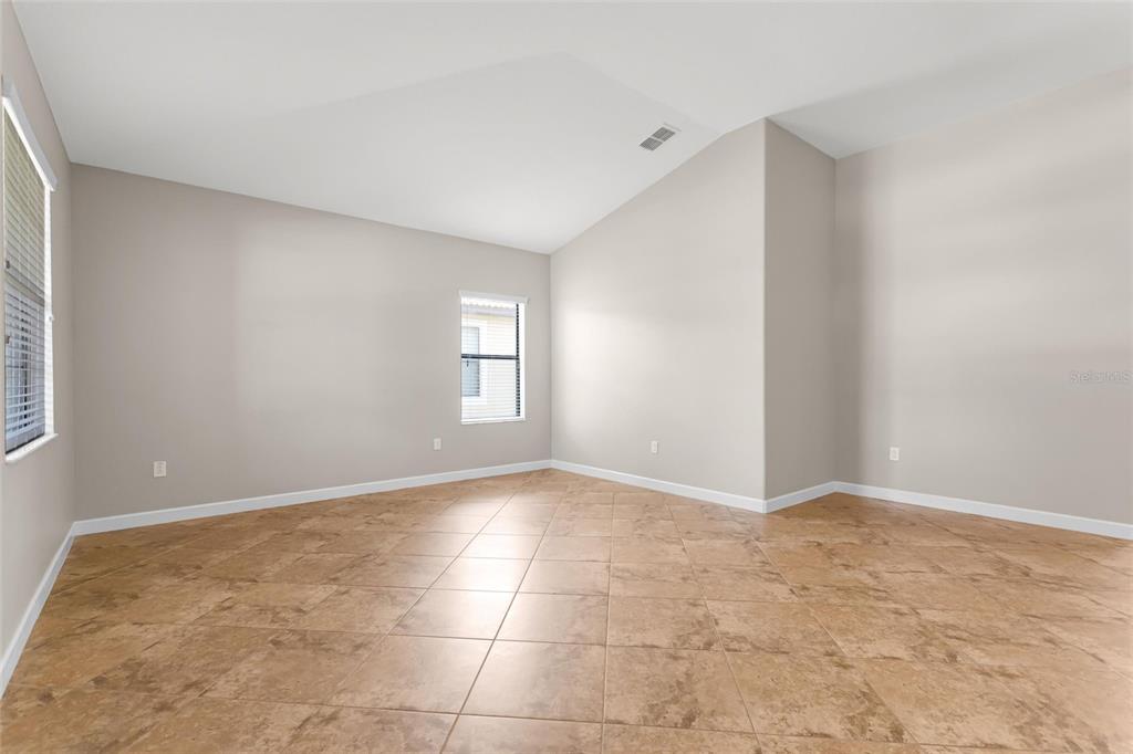 An empty room features light-colored walls, a vaulted ceiling, and tan tile flooring — 1317 GLENEAGLES LN, DAVENPORT, FL