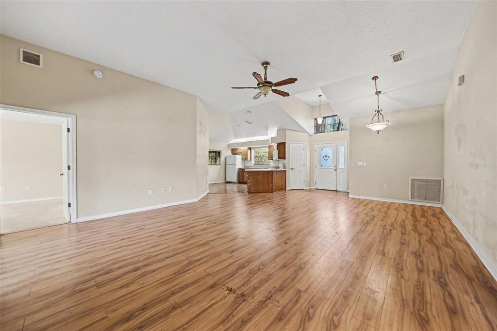 A spacious living room features vaulted ceilings, wood-look flooring, and an open view of the kitchen — 4750 ABACO DRIVE, TAVARES, FL