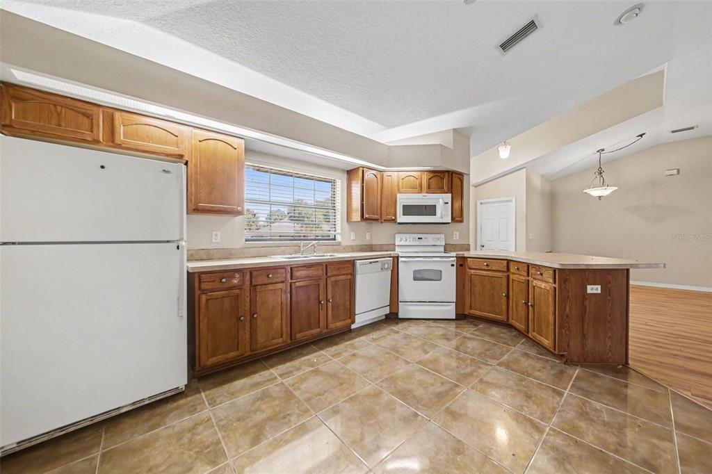 A kitchen features wood cabinets, white appliances, tile flooring, and a breakfast bar — 4750 ABACO DRIVE, TAVARES, FL