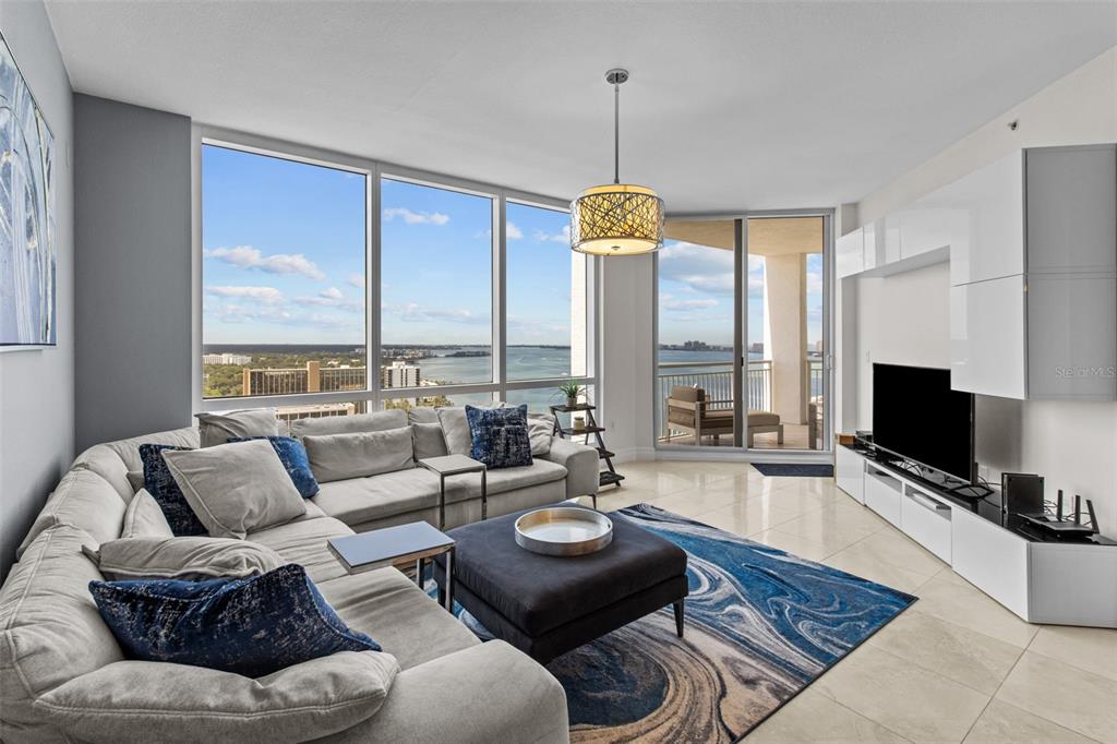 A modern living room features a large sectional sofa, a blue area rug, and floor-to-ceiling windows — 331 CLEVELAND STREET UNIT 2102, CLEARWATER, FL