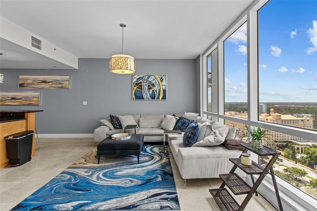 A modern living room features a blue abstract rug, gray sectional sofa, and floor-to-ceiling windows — 331 CLEVELAND STREET UNIT 2102, CLEARWATER, FL